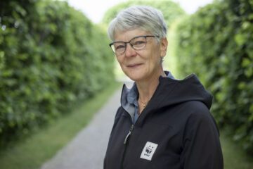 Porträttfoto av Anna Richert med en gång kantad av höga gröna buskar i bakgrunden.