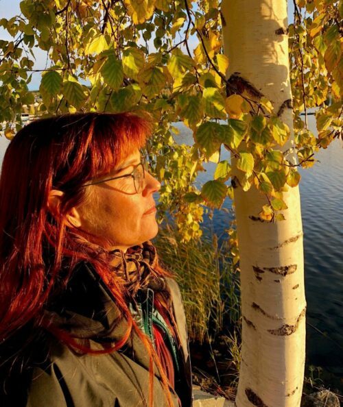 Porträttfoto av Susie Broquist Lundegård. I bakgrunden syns en björk och vatten.