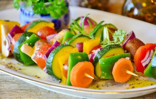 Färgglada grönsaksspett med zucchini, paprika, morot, rödlök, tomat och svamp, kryddade med olja och örter på tallrik.
