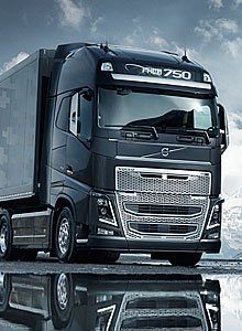 Mörkgrå Volvo-lastbil med hög hytt och släpvagn, speglas i blött underlag. Text: "FH16 750", "VOLVO".