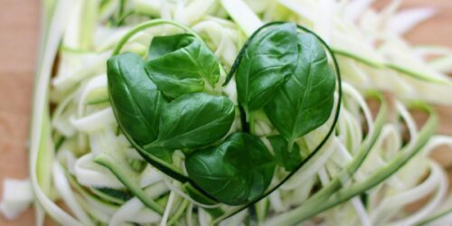 Spiraliserad zucchini i tunna remsor med färska basilikablad arrangerade till ett hjärta.