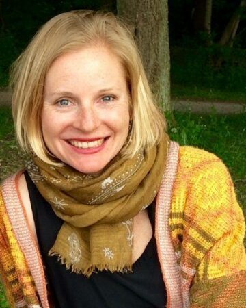 Bild på Jennifer Lenhart. Leende blond kvinna med axellångt hår, grönbrun scarf runt halsen och färgglad stickad kofta.