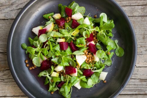 Sallad med machésallat, tärnade rödbetor, päronbitar och linser på en svart tallrik.