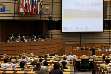 Möte i EU-sal med åhörare och talarpanel; projicerad bild med texten "Beyond GDP".