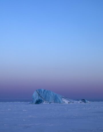 En frusen arktisk landskap med en ensam isberg under en klar himmel som övergår från blå till violett.