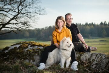Författarna och fotograferna Fredrik Granath och Melissa Schäfer syns sittandes på en stenhäll, med en vit hund sittandes framför Melissa Schäfer.