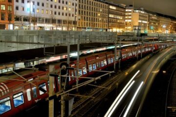 Röda pendeltåg vid en station på natten, ljusspår från ett passerande tåg.