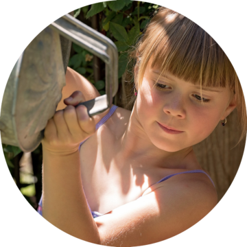 Rund bild: Flicka med blont rakt hår vrider på en metallpump utomhus för att få vatten.