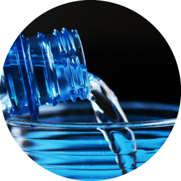 Rund bild: En blå plastflaska häller klart vatten i ett genomskinligt glas.