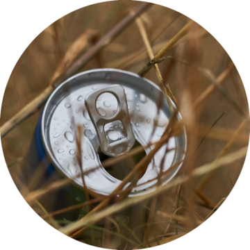 Rund bild: En välkyld, öppnad aluminiumburk med vattenpärlor på locket, omgiven av torra grässtrån.