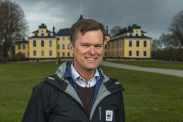 Porträttfoto av Gustaf Lind i en svart jacka med WWF-logga och står framför Ulriksdals slott.