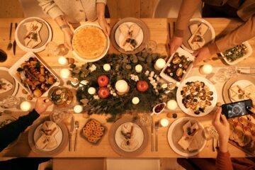 Ett julbord med personer som serverar traditionella svenska rätter, dekorerat med äpplen, ljus och gröna kvistar.