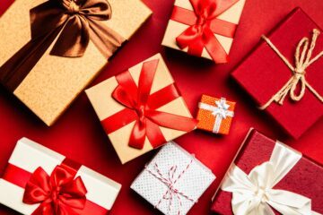 Flera inslagna julklappar i rött, vitt och brunt med röda och vita band på en röd bakgrund.