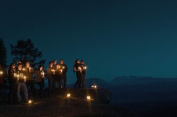 Personer som står med levande ljus på en klippa mot kvällshimlen. Samtliga personer har WWF tröjor med Earth Hour tryck.
