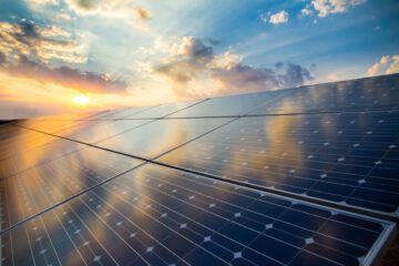 Solpaneler reflekterar himlen med moln och solnedgång, vilket illustrerar solenergi och hållbar energiutvinning.