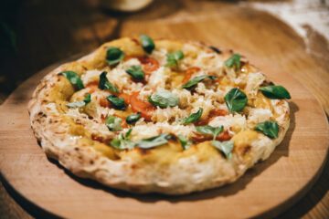 Stenungsbakad pizza, med hummus och grönsaker, på en träbricka.