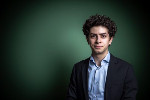 Gaga Jakhashvili Porträttfoto av Gaga Jakhashvili, med lockigt hår och mörk kavaj står framför en grön bakgrund och ser in i kameran.