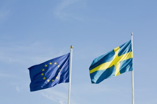 EU-flagga och svensk flagga mot klarblå himmel