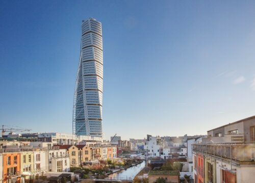 Turning Torso, Malmö Turning Torso i Malmö är en skyskrapa med en distinkt vriden form som sträcker sig högst upp i himlen. På bilden syns Turning Torso mot klarblå himmel med flera låga byggnader runtomkring.