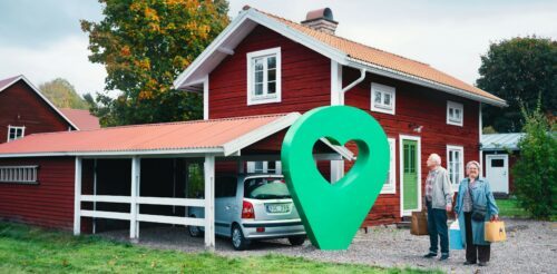 En röd villa med vita knutar, en bil parkerad i garaget och en stor grön kartmarkör med hjärtform i mitten placerad framför huset.