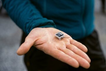 En öppen hand håller en liten elektronisk enhet med en solpanel på ovansidan.