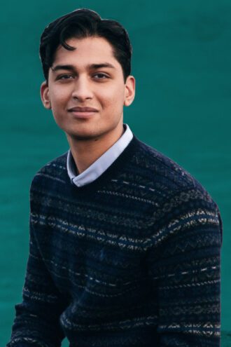 param Porträttfoto av Param Arora med kort mörkt hår bär en mörkblå tröja med mönster och en skjorta under, sittande mot en grön bakgrund.