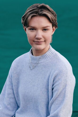 tilde Porträttfoto av Tilde Moberg med kort hår bär en ljusblå stickad tröja och tittar in i kameran. Bakgrunden är enfärgat grön.