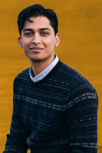Porträttfoto av Param Arora med mörkt hår bär en mörkblå mönstrad tröja och en ljusblå skjorta under, poserar mot en gul bakgrund.