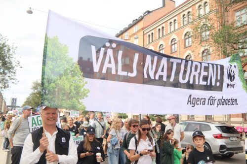 Gustaf Lind i klimatdemonstrationen 2026, på Sveavägen. Han håller i en banderoll med texten "VÄLJ NATUREN Agera för planeten".