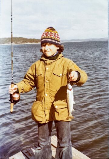 Martin Falklind som liten, han håller ett fiskespö med en fisk på kroken och ler in i kameran.